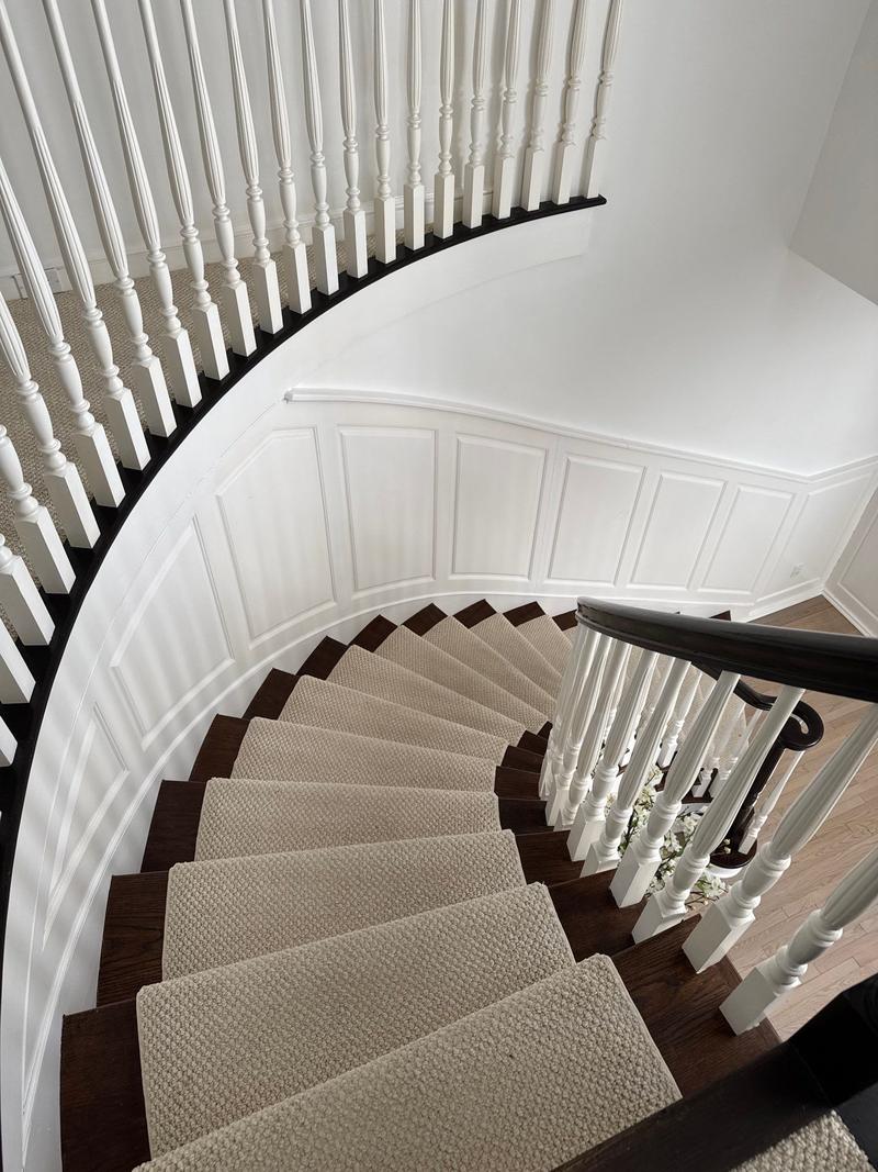 Curved staircase with a carpet runner, white balusters and a dark wood handrail